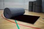 Partially unrolled Air Tumble Track Gymnastics Mat with a black surface, placed on a gym floor for training use.