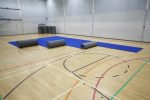 An image of partially unrolled Air Tumble Track Gymnastics Mats with a brown surface, placed on a gym floor for training use.