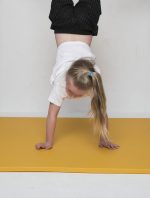 Kid performing a handstand on a cushioned yellow gym mat for training and play.