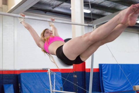 Athlete performing a strength and swing skill on a high bar in a gymnastics facility with padded flooring