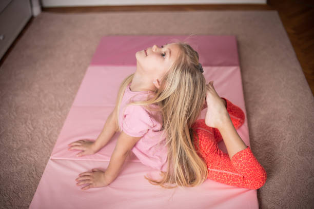 Young girl performing a backbend on a pink AirTumble Foldable Mat in a cozy indoor space, wearing red leggings and a pink shirt